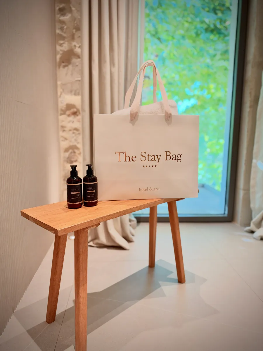 The Stay Bag posé sur un banc en bois, à côté de deux flacons de soin.